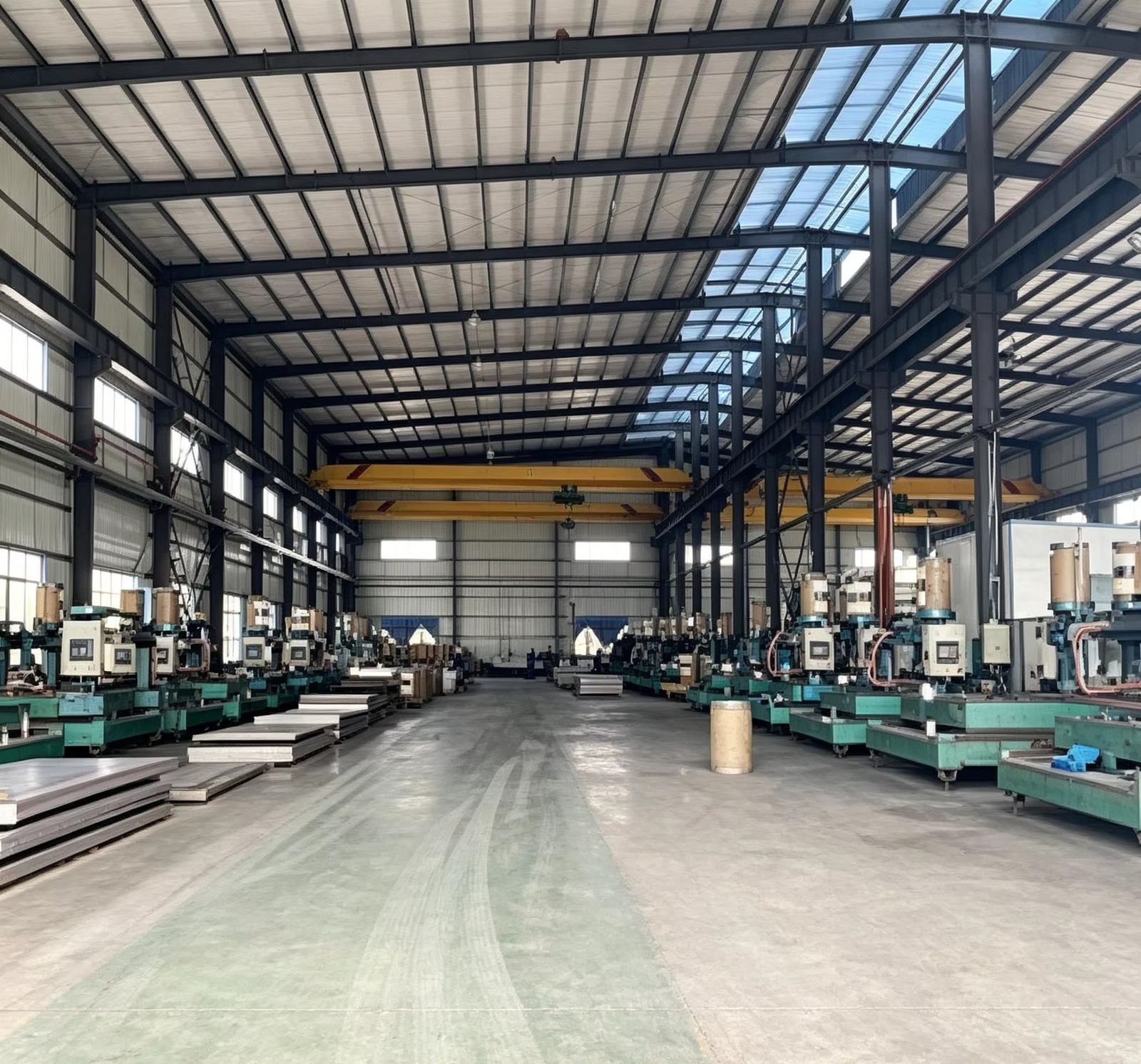Heavy workshop bay with rows of production equipment, an overhead crane and stacked metal sections