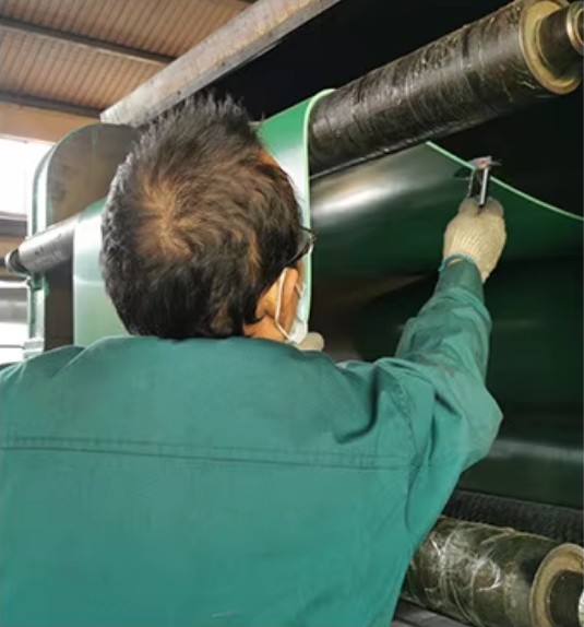 Operator in green workwear steadying the continuous green sheet as it passes over the roller at the feed and take-off station